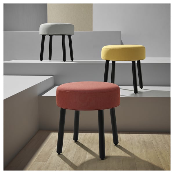 Three colourful, round MÖRTFORS stools in red, yellow, and light blue, each with black legs, arranged in a minimalist, modern setting.