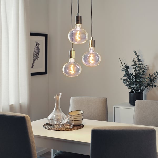 Three glowing MOLNART bulbs above dining table, warm light, minimalist decor.
