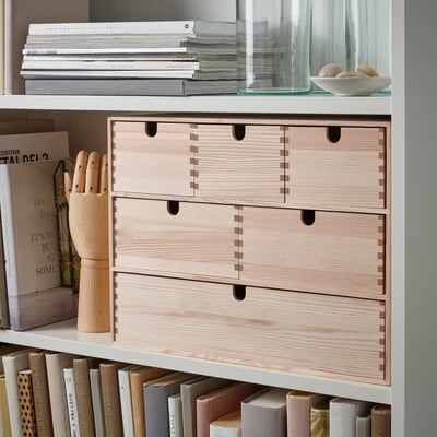 Bookcase with wood drawers and various items including books, a wooden object, and a bowl with sphere objects on the shelves.