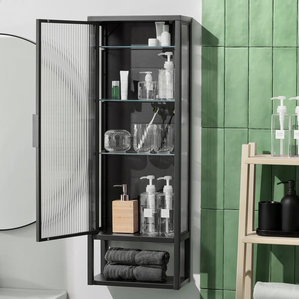 Black wall cabinet with open shelves and reeded glass door, displaying toiletries and towels.