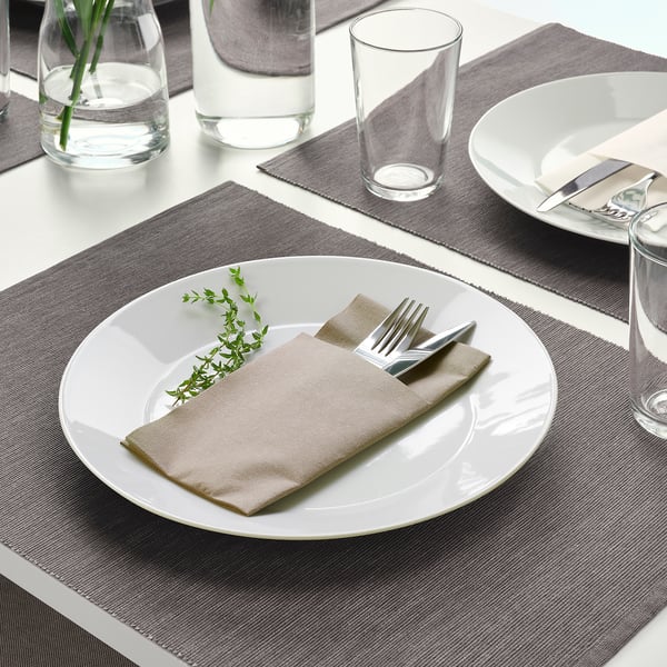 Table setting with white plate, napkin, cutlery, and glass on dark placemat.