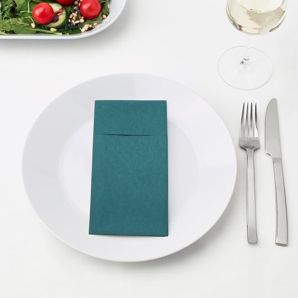 A place setting with a plate, green napkin, fork, and knife. A glass of white wine and salad in the background.