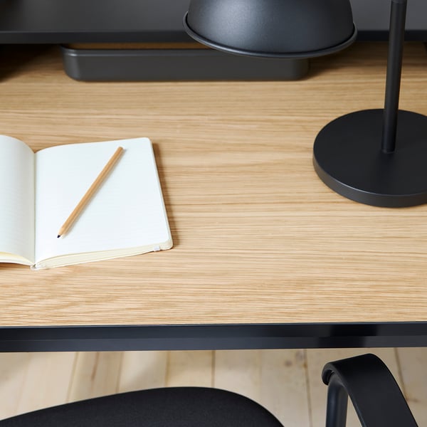 Modern, minimalist desk with natural wood top, black metal base; open notebook and pencil.