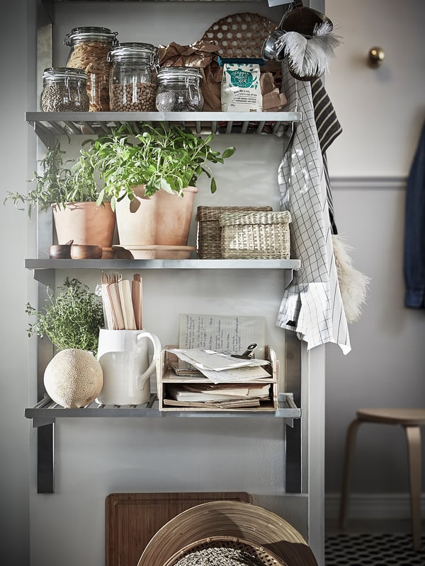 Kitchen shelf setup: pots, jars, recipe books, utensils, herbs, dish towels, on a grey shelf.