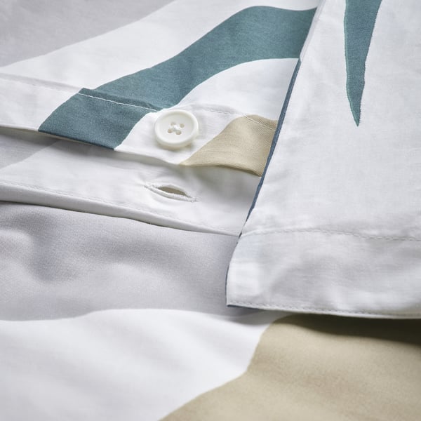 Close-up of a button closure on a white duvet cover with green leaves.