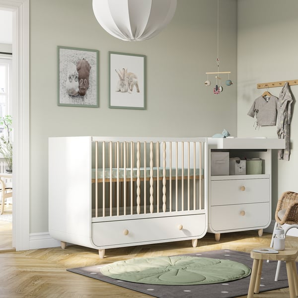 Modern nursery with MYLLRA white cot, green wall prints, hanging light, and changing table. Cot is large, similar to a dresser.