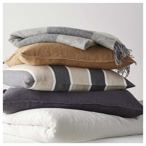 Stack of four pillows in grey, brown, black, and white stripes with a light grey checked wool throw on top.
