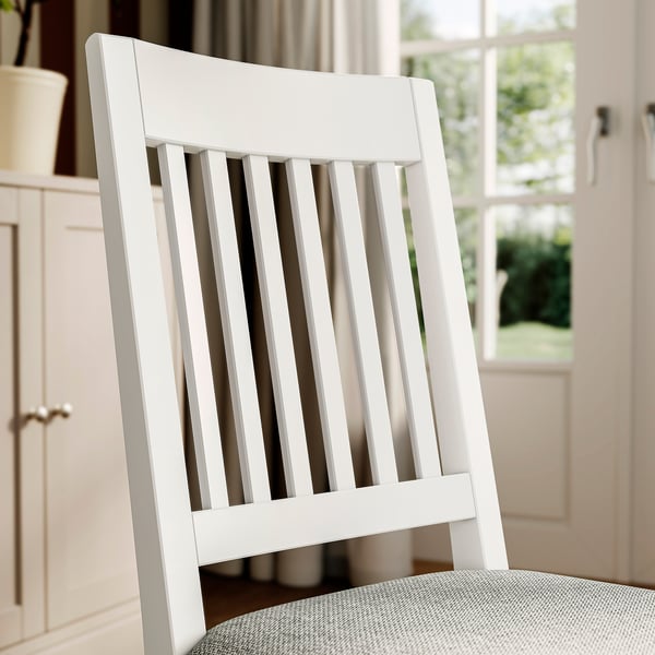 White wooden chair with slatted back and padded seat near window in kitchen.