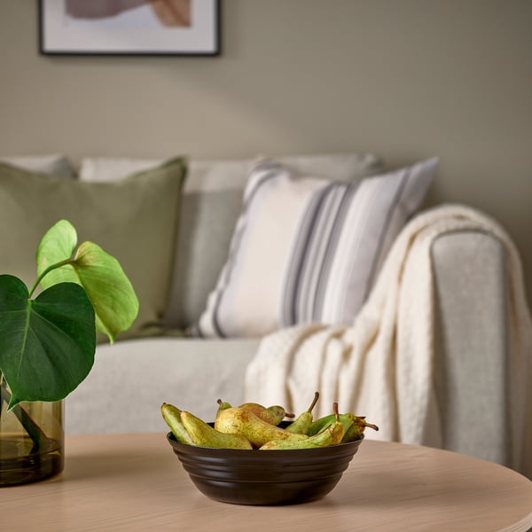 Revolving glass bowl, NÄTBARB, on table near green plant, grey couch with striped pillows.