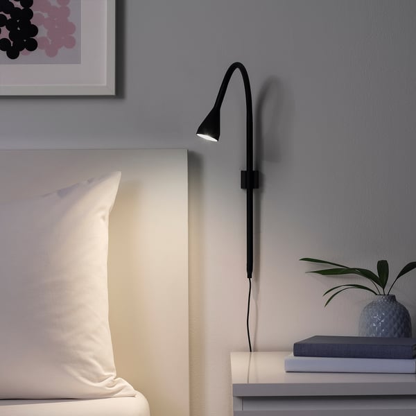 Black NÄVLINGE clamp spotlight on bed, illuminating pillow, sleek & adjustable.