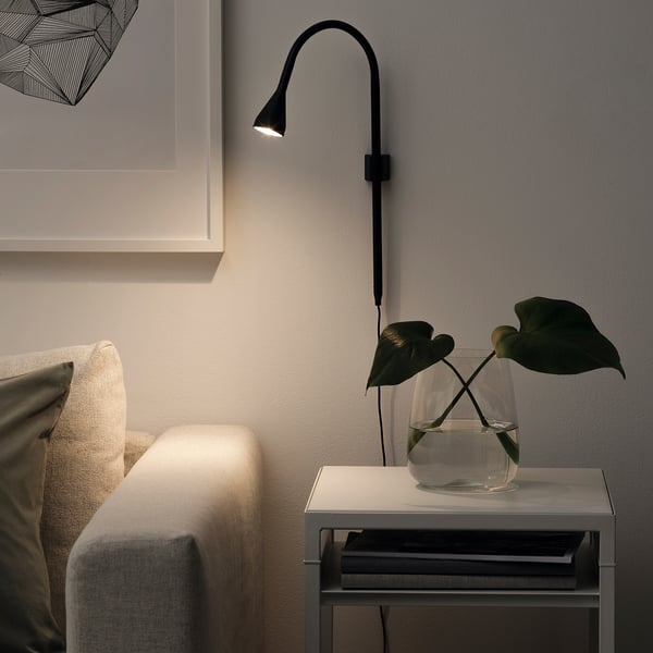 Modern black clamp lamp illuminates table with plant next to muted sofa.