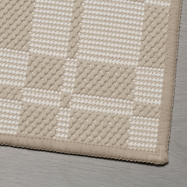 A beige bath mat with a textured, patterned surface and a fabric border, featuring a non-slip backing.