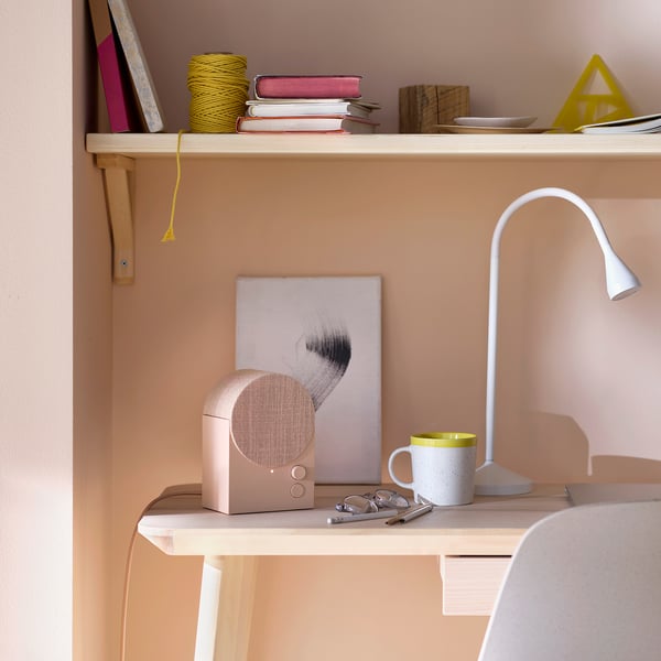 Peach-colored NATTBAD bluetooth speaker on shelf with mug and lamp.