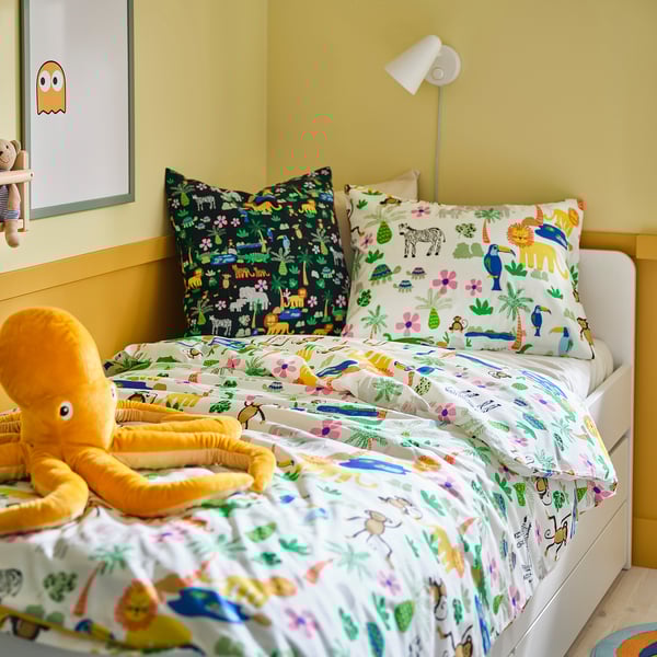 Colourful bed with cushions, octopus, & stuffed toys on bright yellow walls.