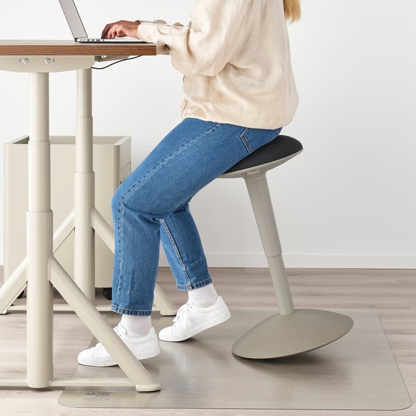 Person using adjustable stool, typing on laptop at a desk with drawers.