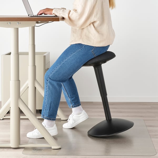 Person sitting on adjustable stool at wooden desk, using laptop.