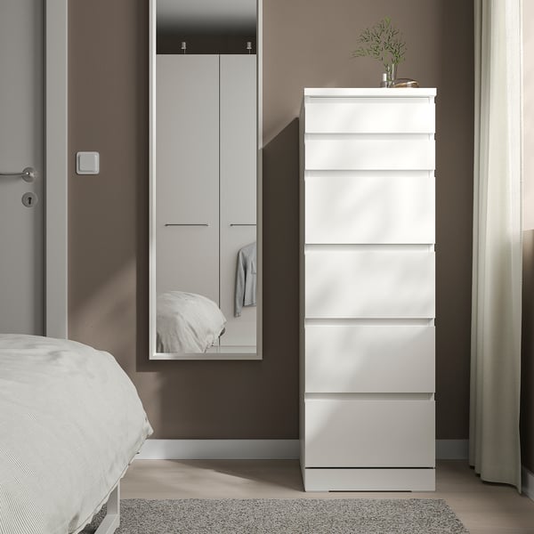 White NISSEDAL chest in bedroom, six drawers, beside tall wardrobe with mirror, sleek design, minimalist decor.