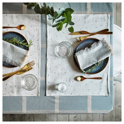 NISSÖGA natural cotton-jute tablecloth, blue-white dishes, gold cutlery, glasses on wooden table with greenery.