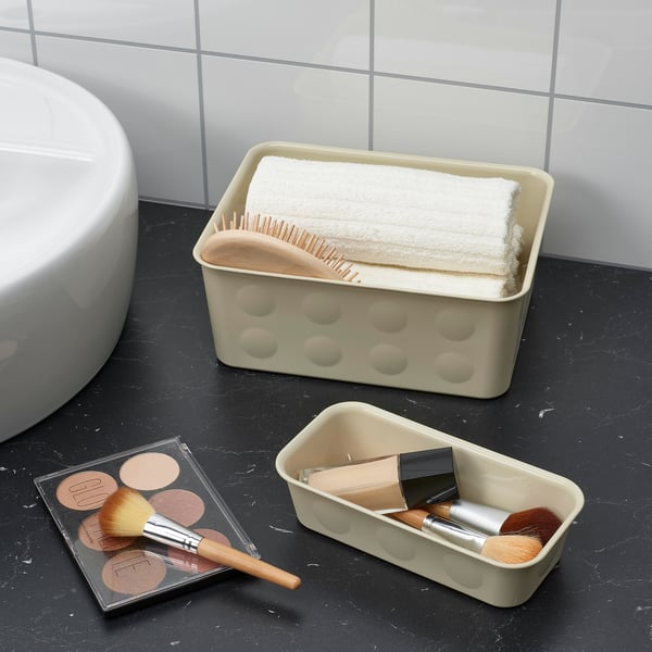 Bathroom counter with organised cosmetics and towels. Two plastic boxes store makeup brushes, foundation, and folded towels, optimising space.