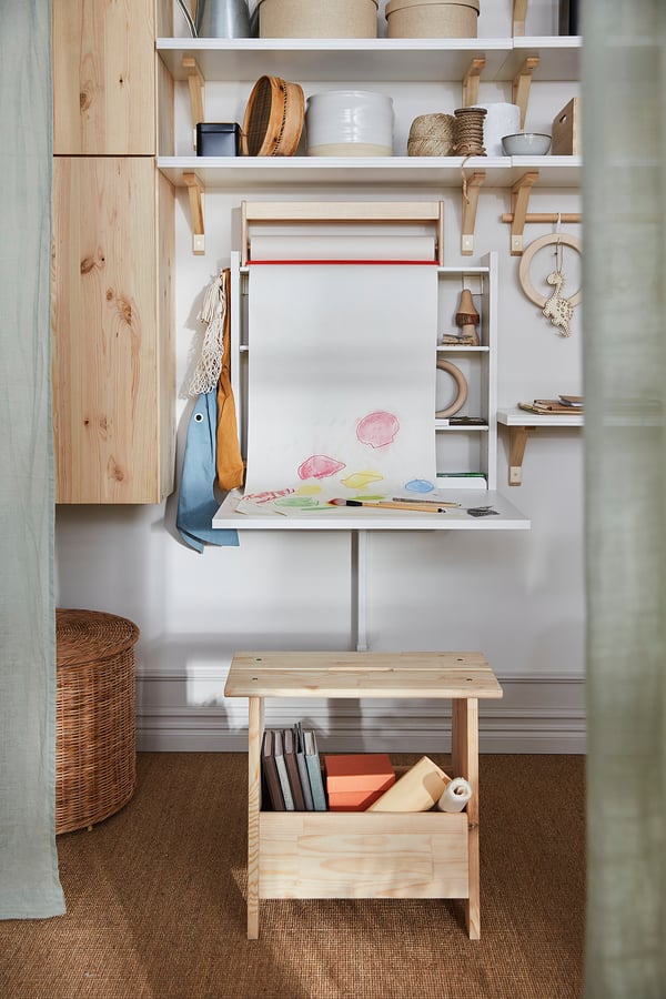 A wall-mounted drop leaf table, NORBERG, light wood. It adjustable shelves and has art supplies on it.