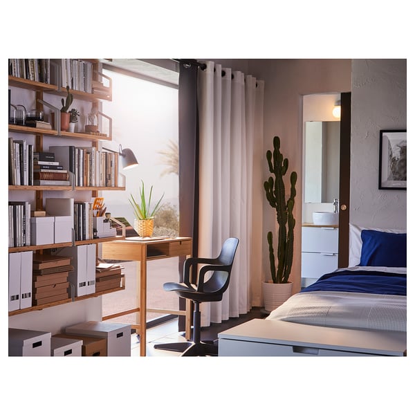 Cosy bedroom with grey curtains, wooden bookshelves, blue bedding, desk, chair, and large cactus.