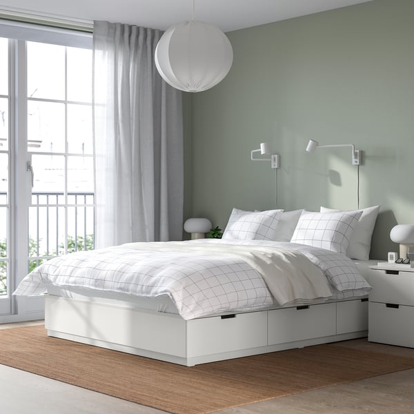 Modern white NORDLI bed with storage drawers and wall lamps.