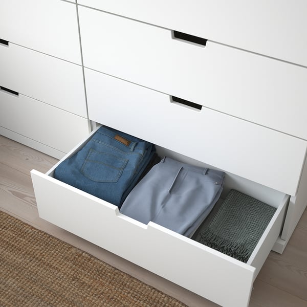 Open NORDLI drawer reveals folded jeans, trousers, and sweater, demonstrating its hidden drawer compartments for organised clothing storage.