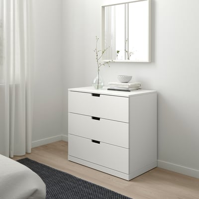 White NORDLI chest with 3 drawers against wall, sleek black handles, bowl & vase on top.