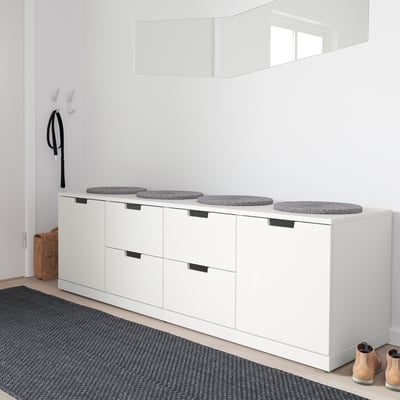 Minimalist white NORDLI chest with cushioned seats, holding four round grey stools, contrasting with a black-and-gray rug and a single tan boot.