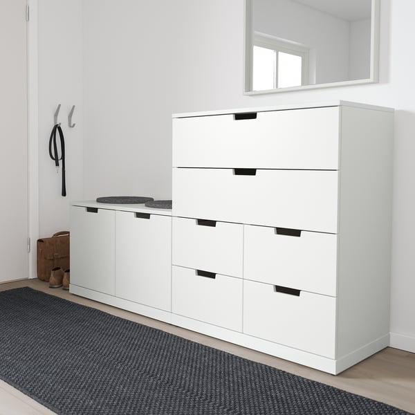 Modern white NORDLI chest in hallway, with grey rug. Tall, six-drawer unit with black handles, placed near hooks and bench.