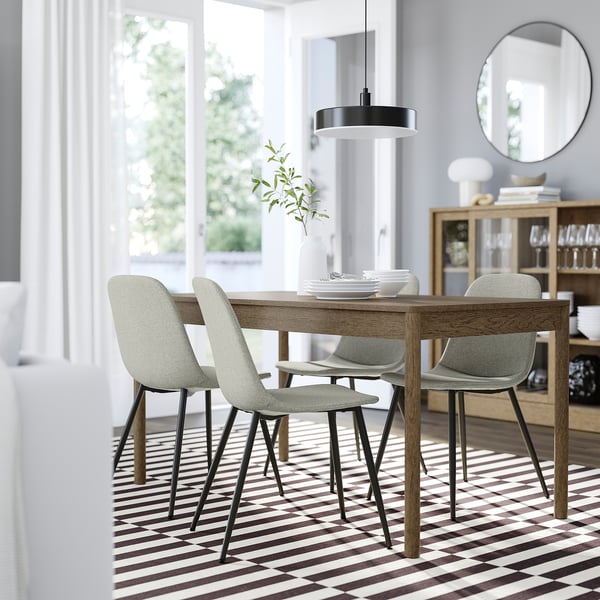 Modern dining room with grey chairs, wooden table, rug, light, sideboard, and large window.
