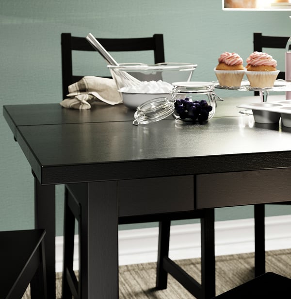 Modern black dining table with two chairs, a bowl of grapes, and cupcakes.