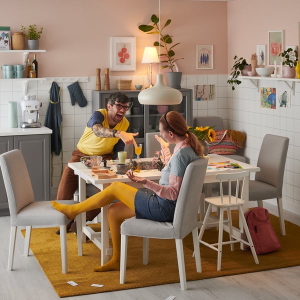 Happy couple enjoying meal at modern NORDVIKEN dining table with gray chairs, pink walls, and cozy decor.