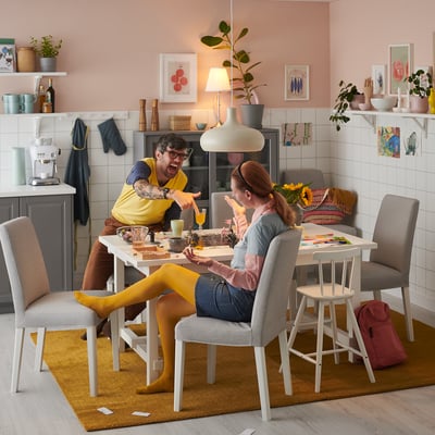 Happy couple enjoying meal at modern NORDVIKEN dining table with gray chairs, pink walls, and cozy decor.