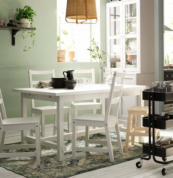 Cosy dining area with white NORDVIKEN table, chairs, rug, potted plants, and hanging lamp.