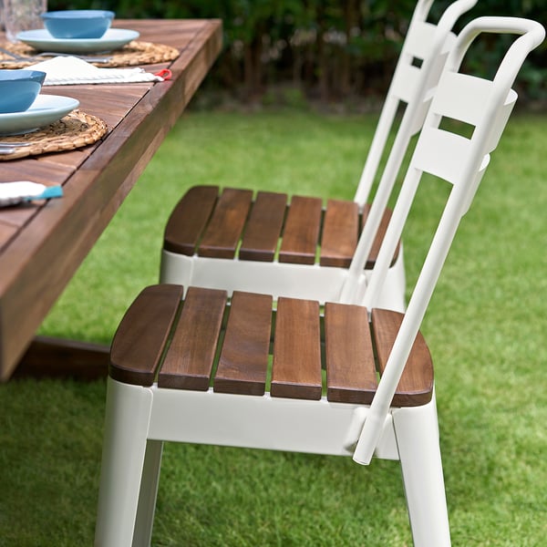 Modern white NORRMANSÖ outdoor chair with wooden seat and back, designed for comfort in a yard setting.
