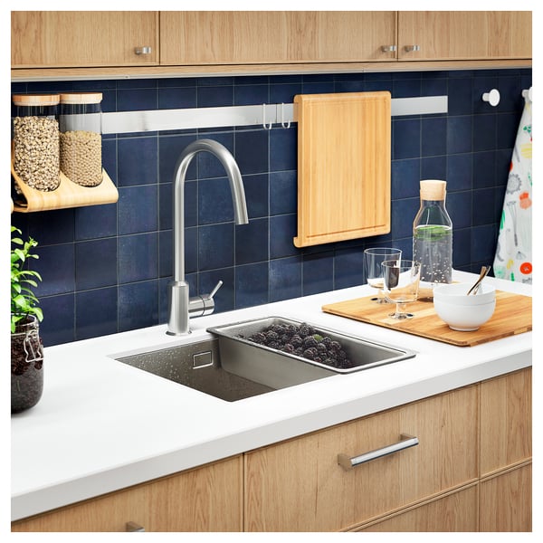 Modern kitchen sink with wood counter, dark tile backsplash, silver tap, stainless colander, jars, cutting board, bowls, glasses.