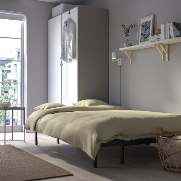 Minimalist bedroom with beige bed, wall-mounted shelf, and hanging garment.