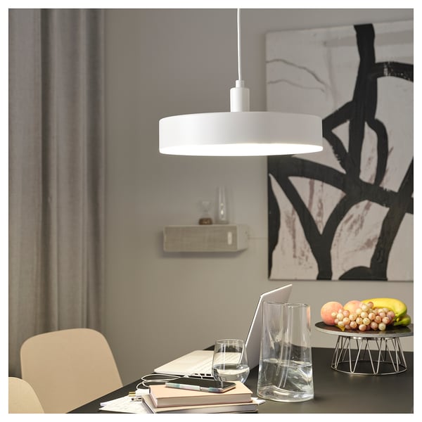 Modern dining table with pendant light, laptop, fruits, and abstract wall art.