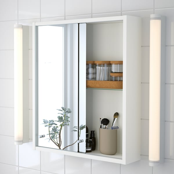 Modern white cabinet with mirror, sliding doors, making contents accessible. Shelves hold makeup and a plant.