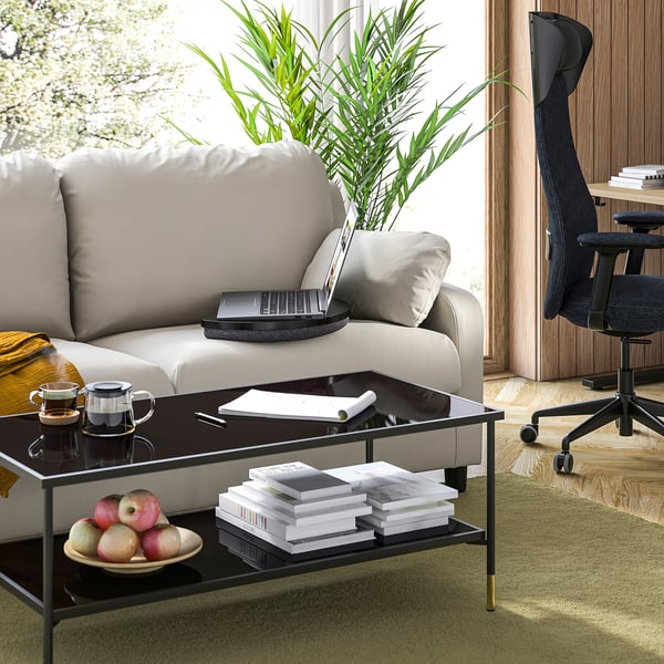 Modern living space with grey sofa, black laptop tray, green rug, and wooden floor.