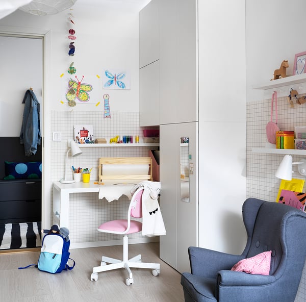 Childs room with white walls, a blue chair, small desk, shelves, and colourful decorations.