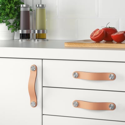 Modern kitchen drawers with leather handles and accessories, including condiments and sliced tomatoes.
