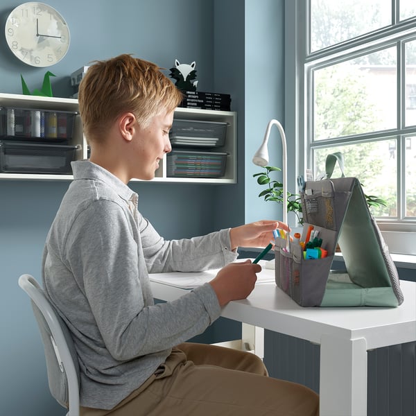 A boy sits at a desk using a laptop; beside the person, an ÖVNING organiser holds school supplies.