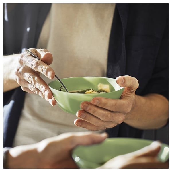 A person holds a green glass bowl of soup, using a spoon. The bowl is modern and inviting, perfect for a cosy meal.