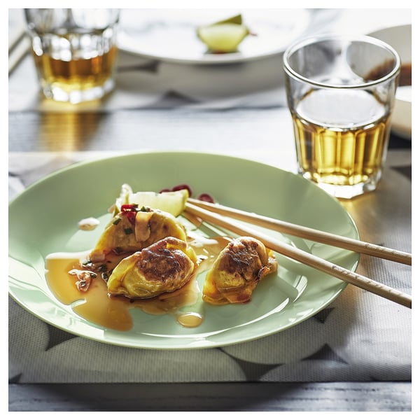 A green glass plate with food and chopsticks, next to two glasses of liquid.