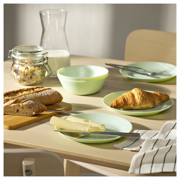 Bright green glass tableware set on wood table, featuring a bowl, plate with bread, and cheese knife. Fresh and inviting breakfast setup.