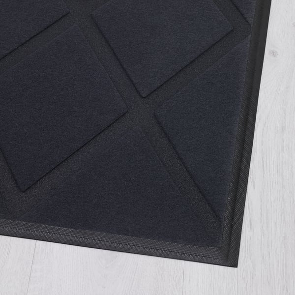 Black door mat with textured polyester surface on light wooden floor.