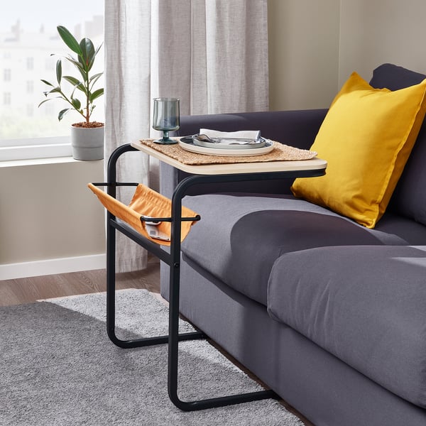 Black OLSERÖD side table beside couch, holding items, plant near window.