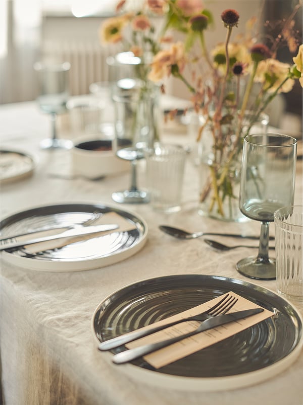 Modern table setting with OMBONAD plates, cutlery, & glassware. Black & white plates, silver cutlery, rustic style.